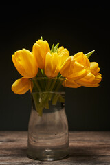 beautiful photo of yellow closed tulip buds in a transparent vase on a black background on a wooden table
