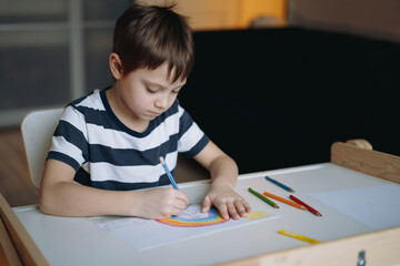 adorable caucasian boy of elementary age drawing with pencils sitting at the desk in his room at home. Image with selective focus