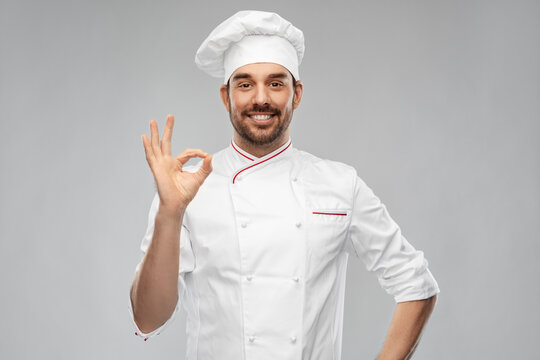 cooking, culinary and people concept - happy smiling male chef in toque showing ok hand sign over grey background