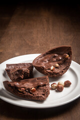Cracked stuffed chocolate and hazelnut easter egg on a white plate on a wooden table.