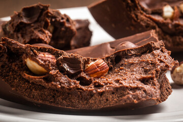Close up of a cracked stuffed chocolate and hazelnut easter egg on a white plate on a wooden table.