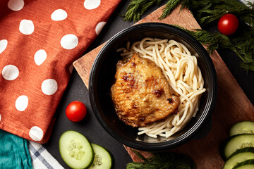 spaghetti with chicken in a black plate on a wooden board with vegetables  top view