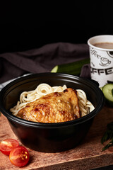 spaghetti with chicken in a black plate on a wooden board with vegetables and coffee