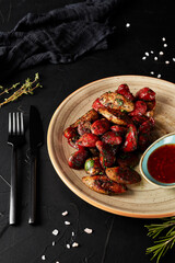 fried sausages with sauce in a brown plate on a black textured background