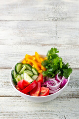 Plate of rainbow salad with different vegetables and herbs in white bowl on white wooden background