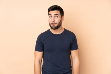 Caucasian handsome man isolated on beige background having doubts while looking up