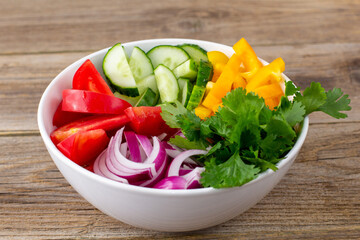 Plate of rainbow salad with different vegetables and herbs in white bowl on wooden background