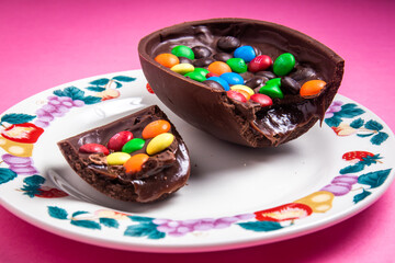 Cracked stuffed mm's easter egg on a white plate with colorful fruit prints on a pink background.