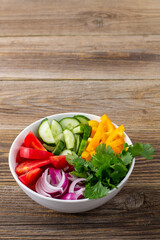 Plate of rainbow salad with different vegetables and herbs in white bowl on wooden background