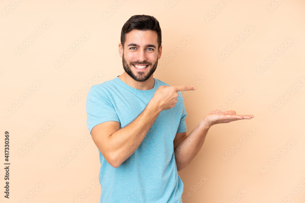 Wall mural Caucasian handsome man isolated on beige background holding copyspace imaginary on the palm to insert an ad