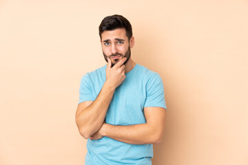 Caucasian handsome man isolated on beige background having doubts