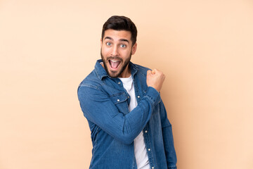 Caucasian handsome man isolated on beige background celebrating a victory