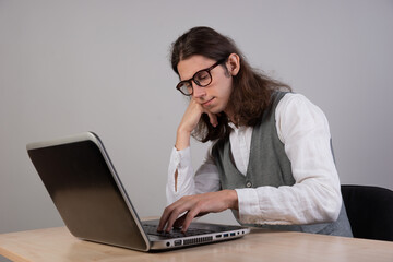 geek guy is trying to write code or learn a new programming language, experience difficulties in the project. A young man with long hair and glasses is working on a laptop