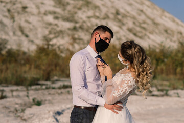 Young loving couple in medical masks in park during quarantine on wedding day.