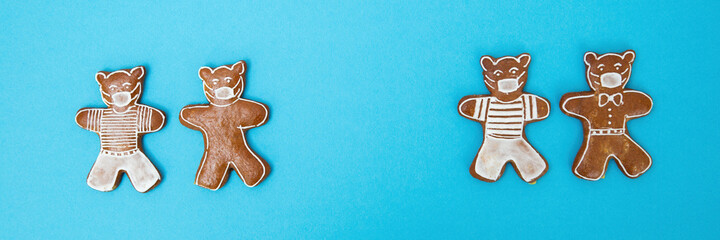 Gingerbread bears with surgical mask on turquoise background. Traditional easter biscuits with coronavirus theme on blue background. Cookies with white icing with covered mouth.