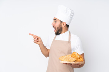 Male baker holding a table with several breads isolated on white background pointing finger to the...