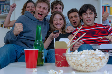 Gruppo di ragazzi e ragazze con birra e pop corn guardano felici la partita di calcio in televisione a casa