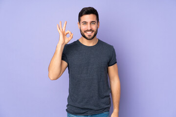 Caucasian handsome man showing ok sign with fingers over isolated purple background