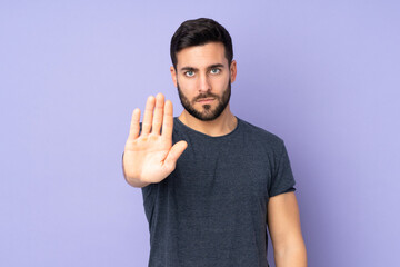 Caucasian handsome man making stop gesture over isolated purple background - obrazy, fototapety, plakaty