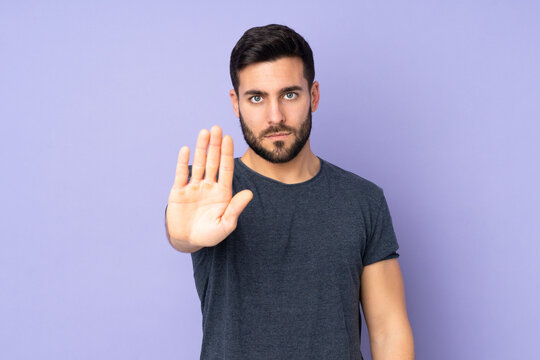 Caucasian handsome man making stop gesture over isolated purple background