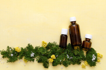 Top view of three brown glass bottles of aroma oils, green grass and flowers on the yellow surface.Empty space