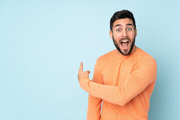 Caucasian handsome man surprised and pointing side over isolated blue background