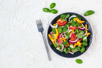 Plate of rainbow salad with different vegetables and herbs on black plate on white stone background