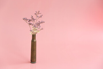 Dried flowers in an empty case from under a firearm on a pink background