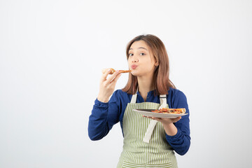 Portrait of young girl in apron eating pizza on white background