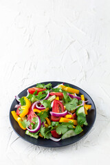 Plate of rainbow salad with different vegetables and herbs on black plate on white stone background