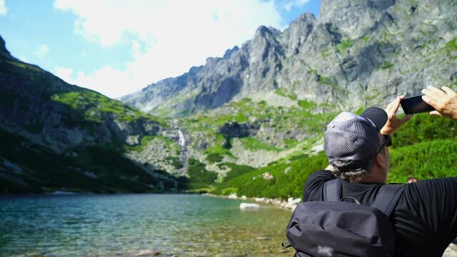 Male tourist uses a smartphone to video a beautiful view in the mountains, Velicke mountain lake, Slovakia, High Tatras