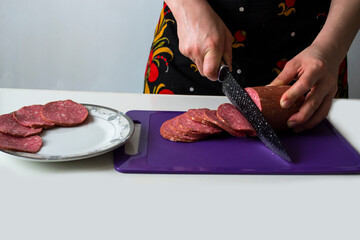 Slicing a sausage loaf with a black knife.