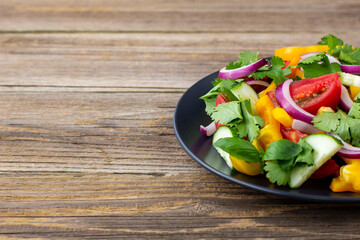Plate of rainbow salad with different vegetables and herbs on black plate on wooden background