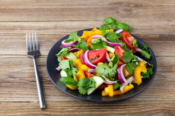 Plate of rainbow salad with different vegetables and herbs on black plate on wooden background