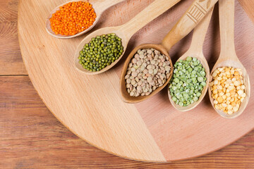Various raw legumes groats in the wooden spoons, top view