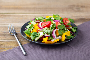 Plate of rainbow salad with different vegetables and herbs on black plate on wooden background