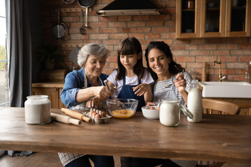 Happy three generations of Hispanic women gather in kitchen cook delicious breakfast together....