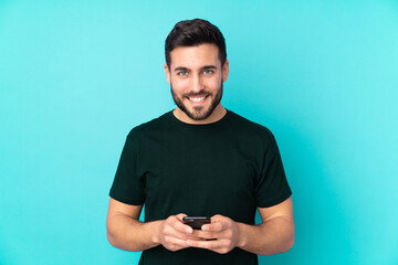 Caucasian handsome man isolated on blue background sending a message with the mobile