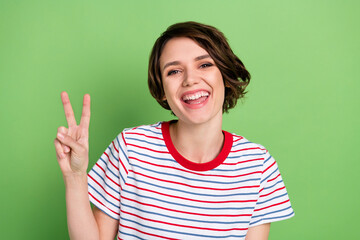 Portrait of lovely cheerful girl having fun showing v-sign isolated over green pastel color background