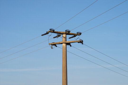 Concrete electric pole with ceramic insulators and voltage lines, in background blue sky with blue sky.