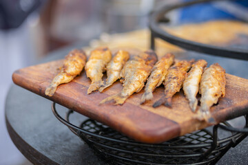 Crispy breaded european smelt fish on wooden cutting board at summer outdoor food market: close up. Seafood, barbecue, gastronomy, cookery, street food concept