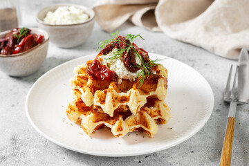 Belgian or Brussels waffles with cottage cheese and dried tomatoes. Homemade waffles in a white plate on the light gray kitchen table. Traditional classic Liege waffles close-up