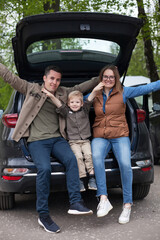Family sitting on  edge of  open trunk of their car
