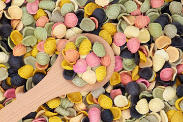 Rainbow arcobalena pasta in a wooden spoon & forming a background. Gluten free & high in vitamins & minerals. Suitable for vegans & vegetarians. Flat lay, top view.