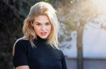 Portrait of a beautiful, blonde woman in black clothes outdoors under warm sunlight