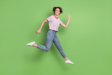 Full length body size profile side view of pretty cheerful girl jumping running waving hi isolated over green pastel color background