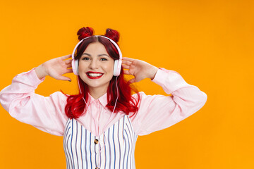 Joyful girl with red hair smiling while listening music with headphones