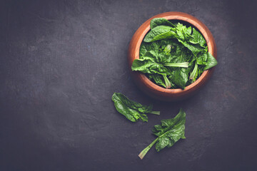 Fresh spinach leaves in a wooden bowl on a dark rustic background. Copy space for graphic design...