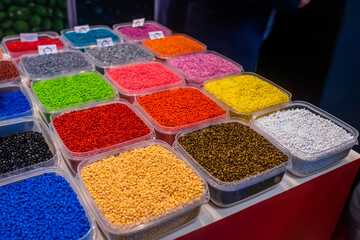 Plastic recycling, renewable resource - heap of colorful secondary polystyrene, polyethylene, polypropylene granules or pellets in containers on table at exhibition, trade show - close up