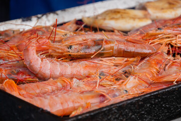 Process of cooking fresh red langoustine shrimps, prawns and squids on grill at summer local food market - close up. Outdoor cooking, barbecue, gastronomy, seafood, cookery, street food concept